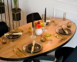 Un dîner élégant est prêt, avec des assiettes sombres, des couverts dorés et des raisins verts. Les art de la table sont mis en valeur par des bougies noires et des fleurs colorées.