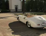 Biały, zabytkowy kabriolet Porsche, udekorowany kwiatami, czeka przed kościołem. To idealny samochod na wesele, gotowy na podróż poślubną.