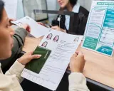 Kobieta z paszportem i formularzem aplikacyjnym czeka na odbiór dowodu osobistego.