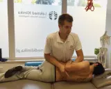 Fizjoterapeuta wykonuje manipulację kręgosłupa pacjenta leżącego na kozetce.