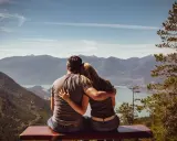 Un couple partage un moment d'amour sensuel, bras dessus, bras dessous, contemplant un paysage montagneux et un lac paisible.