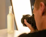 Un fotografo cattura la foto luce di una bottiglia bianca, illuminata da un pannello luminoso.