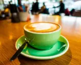 Ein cremiger Cappuccino mit doppeltem Espresso, kunstvoll verziert, in einer leuchtend grünen Tasse auf einem Holztisch.