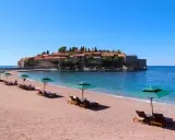 Ein idyllischer montenegro sandstrand mit Liegestühlen und Sonnenschirmen, im Hintergrund die malerische Insel Sveti Stefan.