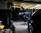 Mechanik bada przyczynę, dlaczego auto nie odpala. Podniesiony przód pojazdu i widoczny silnik sugerują skomplikowaną usterkę.