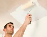 Hombre pintando el techo con rodillo. Se ve la mano sujetando el rodillo y la pintura blanca aplicándose.