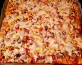 Pyszne, prostokątne ciasto na pizzę z suchych drożdży, obficie posypane kurczakiem, kukurydzą i serem.