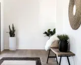 Przytulny przedpokój w stylu boho z drewnianą ławką, plecionym lustrem i roślinami.