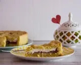 Slice of crostata with ricotta and jam on a yellow polka dot plate, with a whole crostata in the background.