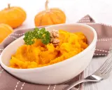 Un tazón de cremoso **puré de calabaza al horno**, adornado con perejil y nueces. Al fondo, calabazas pequeñas y una servilleta marrón.