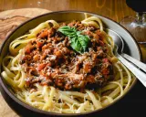Schüssel mit Spaghetti und herzhafter Bolognese-Sauce, garniert mit Basilikum und Parmesan. Ein klassisches italienisches Gericht, das Lust auf mehr macht.