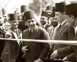 Männer in traditionellen orientalischen Filzhüten bei einer Zeremonie. Einer schneidet mit einer Schere ein Band durch.