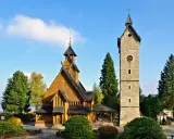 Drewniany kościółek i kamienna wieża z zegarem, jedne z głównych atrakcji Karpacz i okolice, na tle błękitnego nieba.