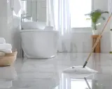 Czyszczenie łazienki w toku. Mop delikatnie przesuwa się po lśniącej podłodze, a stos białych ręczników czeka w wiklinowym koszu.