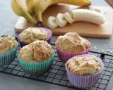 Fünf leckere bananenmuffins ohne zucker in bunten Förmchen auf einem Gitter. Bananen und Mehl im Hintergrund.