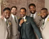 Groomsmen in light tan suits and one in a dark green suit, all smiling. They are dressed for a wedding, showing when grooms get suits.