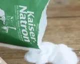 Kaiser Natron wird zum Teppich reinigen mit Natron verwendet. Das weiße Pulver liegt auf Holz.