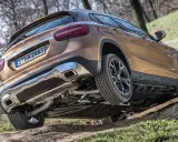 Złoty Mercedes GLA 220 4MATIC pokonuje nierówny teren, unosząc jedno koło.