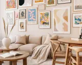 Un salón moderno con un sofá beige y una colección de cuadros para encima del sofá, llenos de color y formas abstractas.