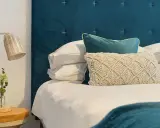 Cabecero de tela azul con cojines y lámpara de mimbre. Si buscas como limpiar cabecero de tela, este es un ejemplo de cómo mantenerlo impecable.