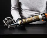 Ręce w czarnych rękawiczkach aplikują czarny silikon K2 na część pompy wodnej. Zastanawiasz się, ile schnie silikon? Ten produkt jest odporny na wysokie temperatury.