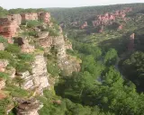 Impresionante cañón con formaciones rocosas rojizas y vegetación frondosa, típico de las áreas protegidas de Castilla-La Mancha.