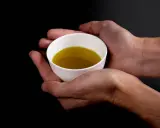 Mani che sorreggono una tazzina bianca con olio evo. Il suo significato è prezioso, un nettare dorato.