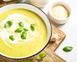 Aksamitny zupa krem z cukinii, udekorowana listkami bazylii i startym parmezanem, podana z czosnkiem i łyżką.
