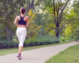 Donna corre su un sentiero nel parco, godendosi la sua zona 2 corsa tra gli alberi verdi.