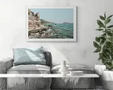A framed print of a coastal scene, reminiscent of fine art photography galleries, hangs above a sofa. The artwork depicts a rocky shoreline with people relaxing under umbrellas.