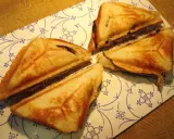 Goldbraune Bananen-Toast-Sandwiches, dreieckig geschnitten, liegen auf einem Teller mit blau-weißem Muster.