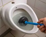 Hand uses a plunger to clear a toilet bowl, tackling stubborn Urinstein im Rohr entfernen.