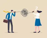 Un hombre y una mujer intentan comunicarse con latas y cuerdas, pero el mensaje se enreda, ilustrando la falta de comunicación efectiva.