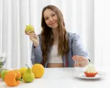 Dziewczyna trzyma jabłko, odrzucając ciastko. To ilustracja zasad postu przerywanego.