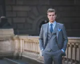 A man in a sharp grey suit, vest, and blue tie exemplifies formal cocktail attire for men, ready for any elegant event.