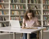 Młoda kobieta uczy się w bibliotece, zastanawiając się, czy studia chemiczne to dobry wybór.