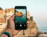 Dłoń trzyma smartfon, na ekranie którego widać malowniczą włoską wioskę nad morzem. Chcesz wiedzieć, jak ulepszyć aparat w telefonie? Oto przykład pięknego ujęcia!