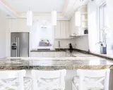Plan de travail en granit, un danger potentiel pour les couteaux de cuisine. Cuisine moderne avec réfrigérateur, armoires blanches et tabourets.