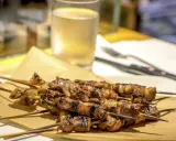 Arrosticini, uno dei piatti tipici abruzzesi, serviti su carta paglia con un bicchiere di vino bianco sullo sfondo.