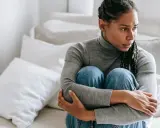 Donna seduta sul letto, abbracciata, con espressione preoccupata. Sembra soffrire di ansia da separazione dal partner.