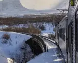 Tåg luleå narvik färdas genom ett snöigt landskap med berg i bakgrunden.