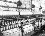 Macchinario industriale per la filatura con fili avvolti su bobine e grandi rulli.