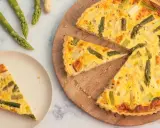 Herzhafte Spargel Quiche mit frischem Spargel, goldbraun gebacken. Ein Stück auf einem Teller, der Rest auf einem Holzbrett.
