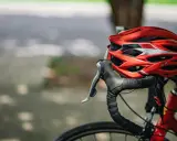 Czerwony kask rowerowy i kierownica z owijką. Niezbędne wyposażenie rowerzysty na bezpieczną podróż.