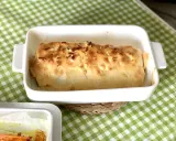 Bacalao gratinado con alioli, cubierto de almendras tostadas, en una fuente blanca sobre mantel de cuadros verdes.