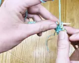 Manos tejiendo punto ojo de perdiz con hilo turquesa y agujas de madera.