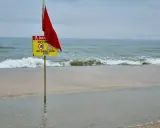 Röd flagga och skylt varnar för farliga strömmar vid stranden i Goa, Indien. Ingen badzon.