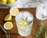 Orzeźwiający gin i tonic z plasterkiem cytryny i gałązką rozmarynu, otoczony świeżymi cytrynami.
