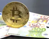 Moneda de Bitcoin sobre billetes de euro. El futuro del euro digital podría ser así.