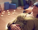 Kvinna med ögonbindel vilar under brahma yoga, omgiven av levande ljus och yogablock.